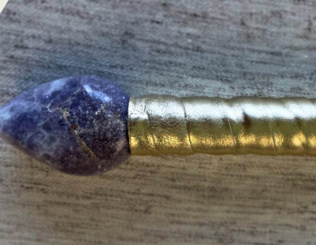 Close view of a faceted violet pommel stone set at the base of a gold-wrapped handle