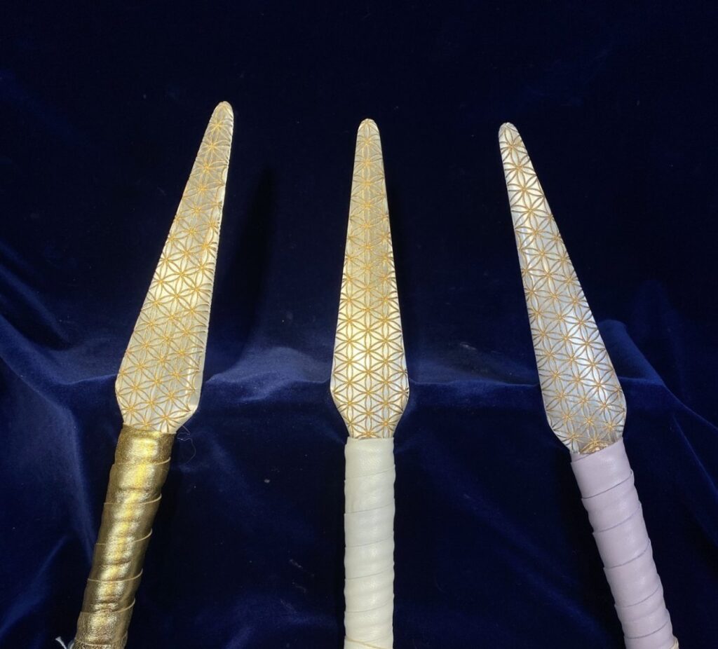 Three Flower of Life selenite swords laid out upright on deep navy velvet, blades engraved edge to edge, each with a different handle wrap